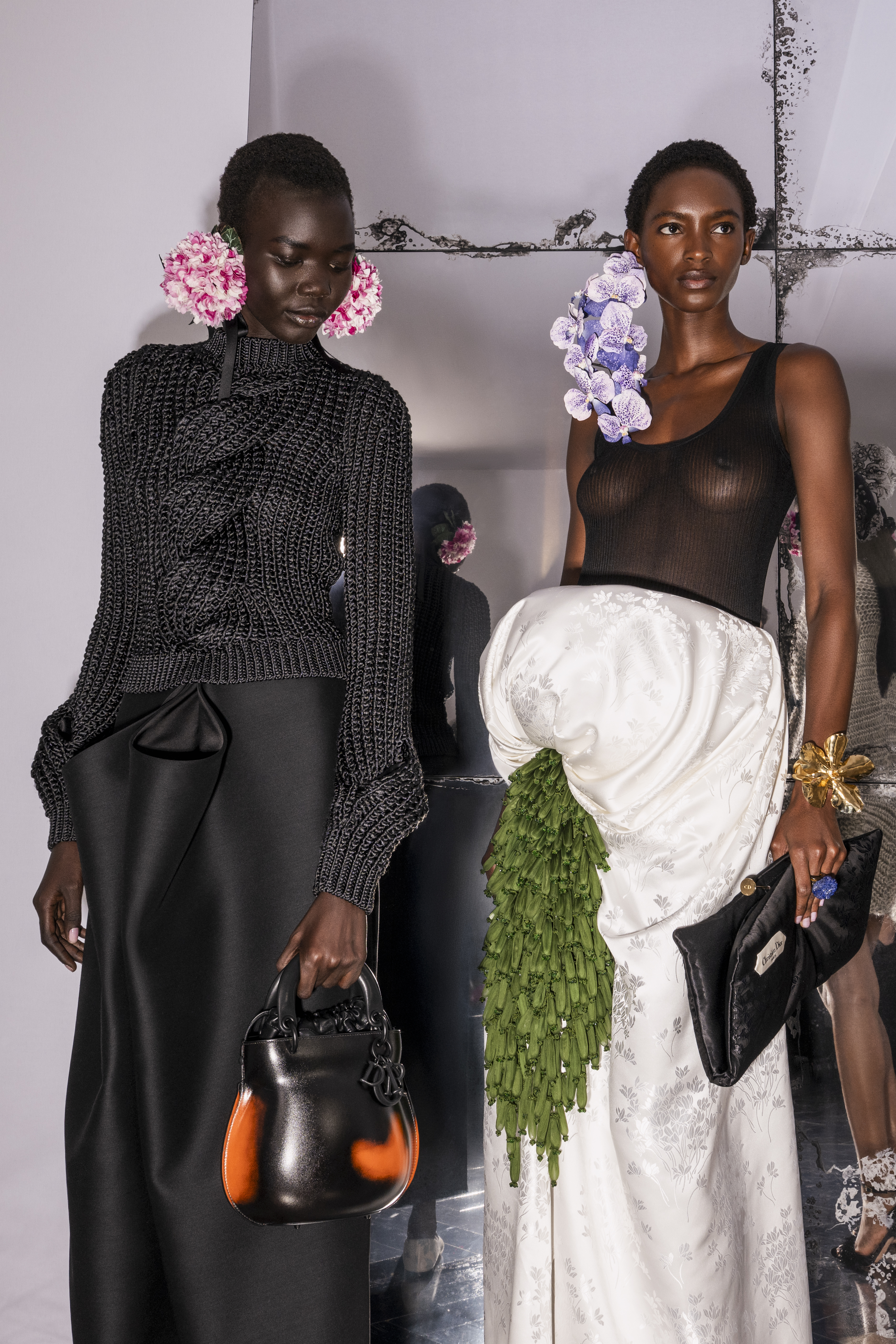 POISON Black cable-knit sweater worn with a long straight skirt in black wool, protruding at the front in two satin-lined stiff open  gathers. FOUGÉRE Rib-knit tank top in black silk, ecru jacquard skirt with cyclamen motif, asymmetrically draped and held by a boned construction at the hip, enhanced with a vegetal cluster of forest green shibori organza 